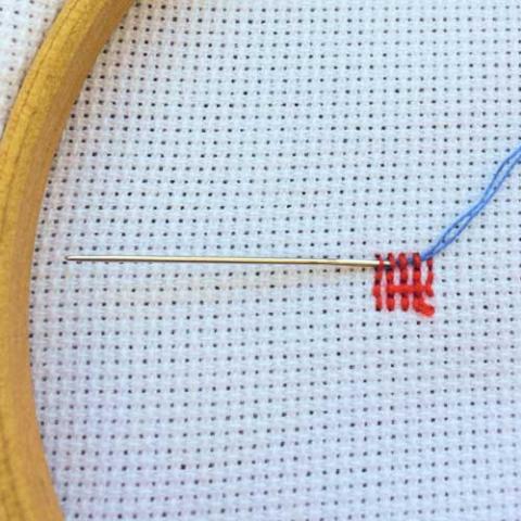 Photo of fabric in an embroidery hoop with some basic stitches in red thread. 