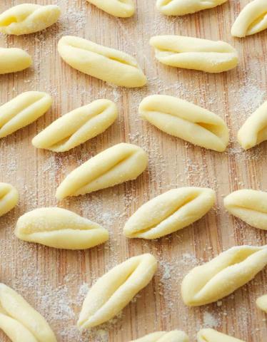 Image of a brown wooden table dusted in flour covered in freshly rolled cavatelli pasta.
