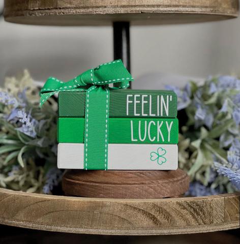 Image of 3 pieces of wood painted different colors with words on the spine to look like a stack of books tied with a bow. . 