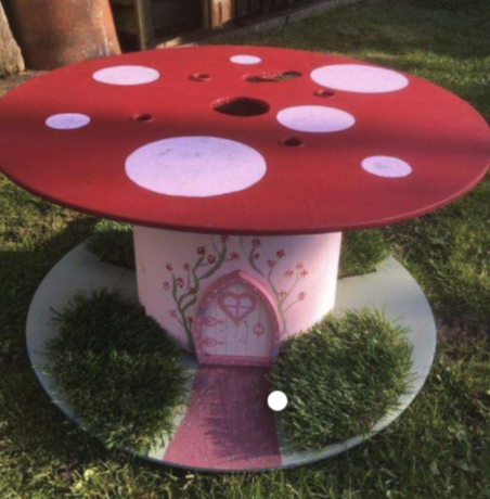 3-D Printer Spool that is painted and decorated to look like a red toadstool house with bushes glued down on the bottom, which is painted green.