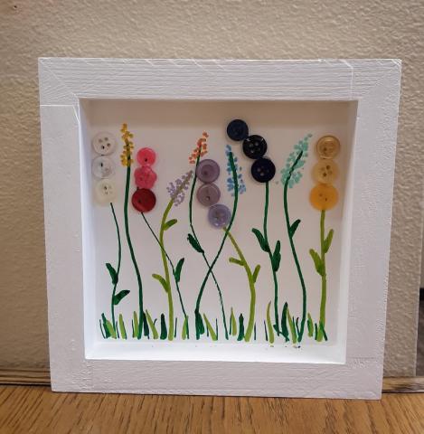 Image of the craft featuring a painted wooden box frame with flowers made of buttons and painted stems. 