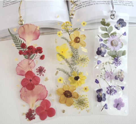 Three bookmarks, the left with red flowers on them, the middle with yellow, and the rightmost with purple flowers on it. All rest on a book.