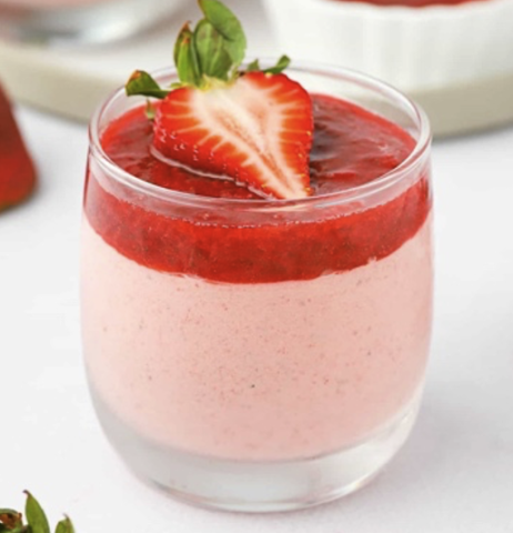 A cup of strawberry mousse and a singular strawberry at the top.