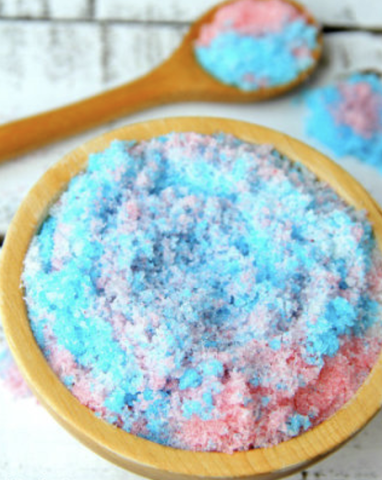 Blue and pink sugar scrub soap on a wooden dish and a wooden spoon.