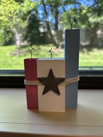 Image of the craft featuring 3 colored blocks of wood painted red, white & blue and tied together with twine wires coming out of the top to look like fireworks 
