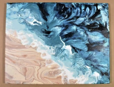 Beach painting of a wave on sand made using a paint-pour technique.