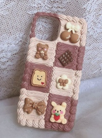 A phone case with small cute items on it such as a chocolate bar, teddy bear, brown bow, a small toast with a heart on it, brown cherries, etc.; all arranged in a quilt-like pattern.