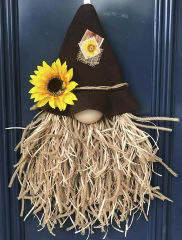 A gnome head made of a straw beard, and brown felt hat, and with a sunflower on the hat, hung on a blue door.