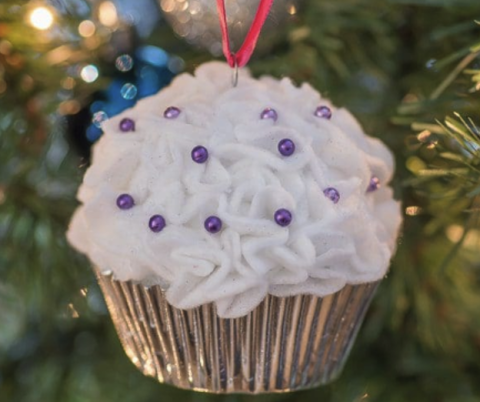 A cupcake ornament hanging on a tree by a red string, with purple bead sprinkles on white cloth frosting.
