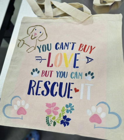 Tote bag with a dog, paws, and flowers painted on it as well as the words "you can't buy love but you can rescue it"