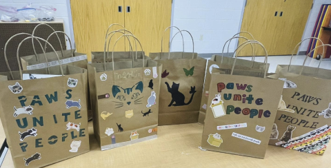 7 brown paper bags with cat stickers and lettering on it, with the words stating "paws unite people."
