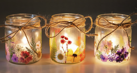Image of the craft featuring small mason jars with pressed flowers glued to the outside of the jar and a tea light candle inside. 