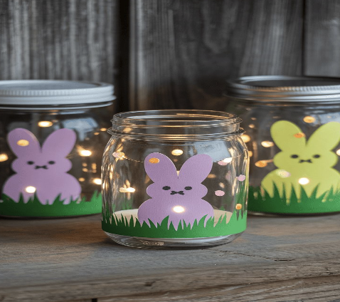 3 jars with grass cut outs and purple/yellow bunny peeps on them, all resting on a wood table with a wood backdrop.