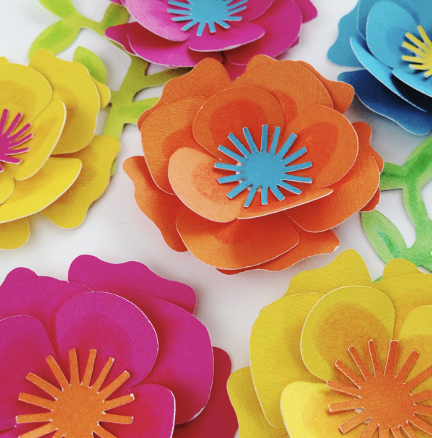 Orange, yellow, pink and blue paper flowers on a white surface.