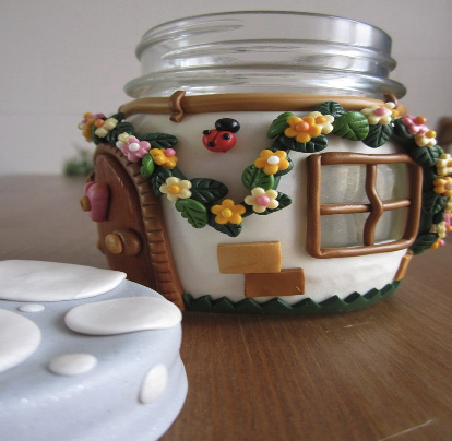 Clay fairy house that is white with brown doors, ladybug, flowers and vines sculpted on it.