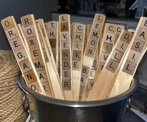 Scrabble Plant Markers in a metal pot, all having different plants spelled on the markers in scrabble letters.