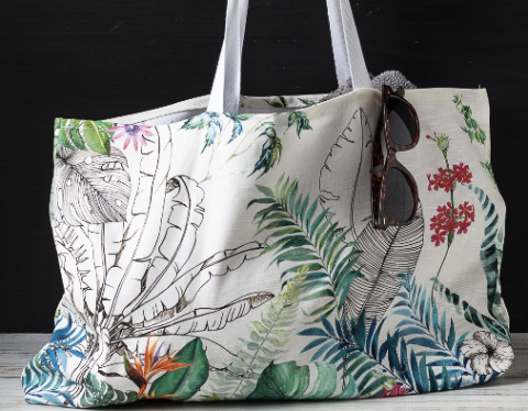 Beach bag with plants on it, and brown sunglasses hanging off of it.