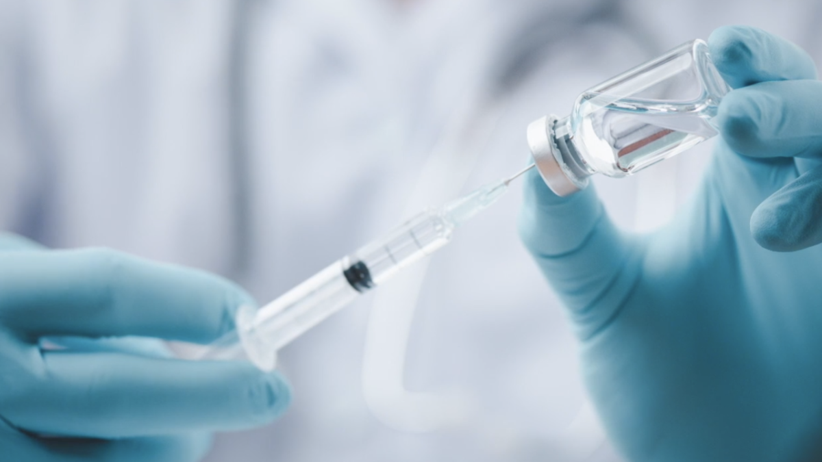 Photo of medical personnel with gloves using a syringe to get medicine out of a vial.