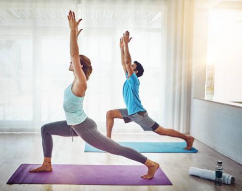 Man and woman in profile standing on Yoga mats in a standing Yoga pose. 