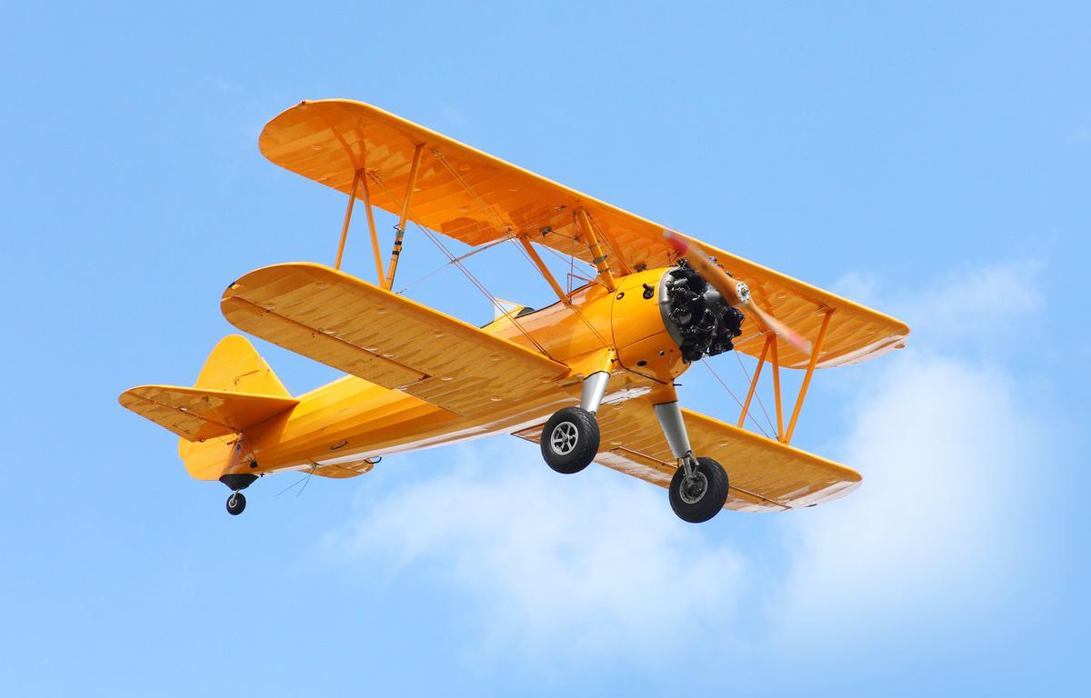 Vintage yellow glider plane flying in the sky.