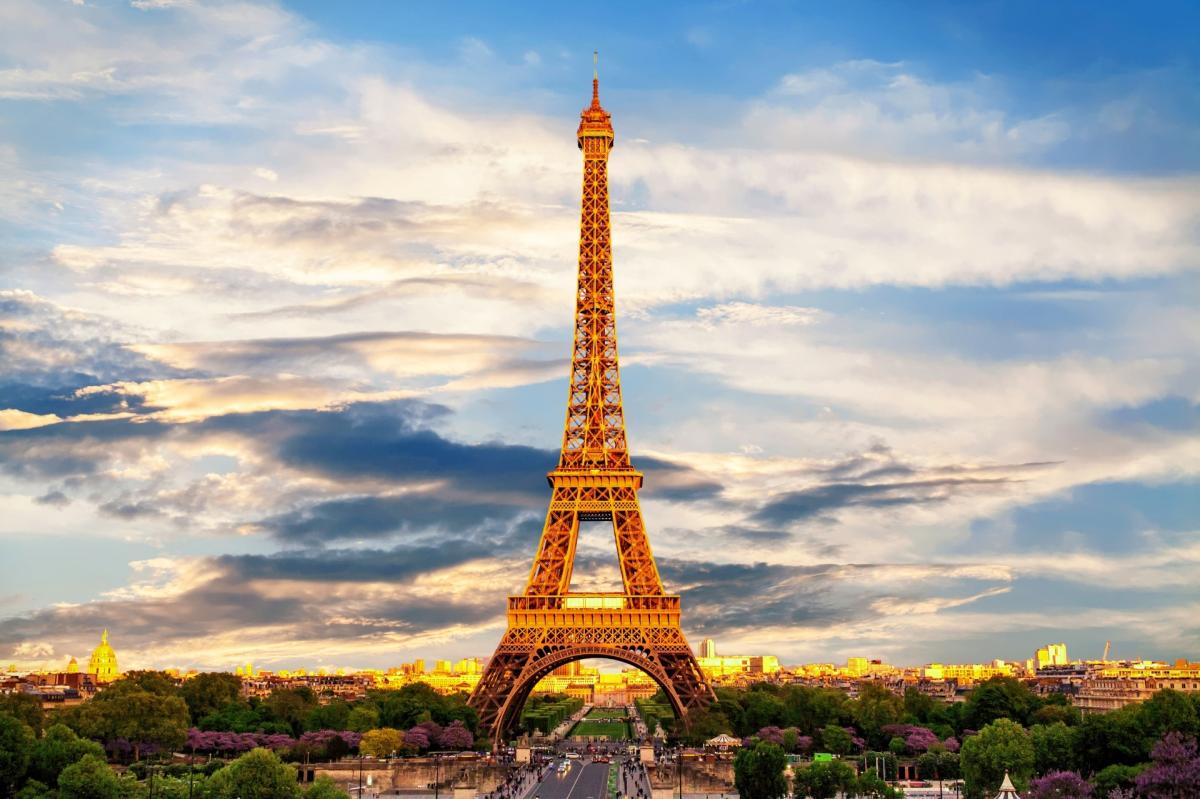 Image of the Eiffel Tower centered in front of a blue sky above the Paris streets.