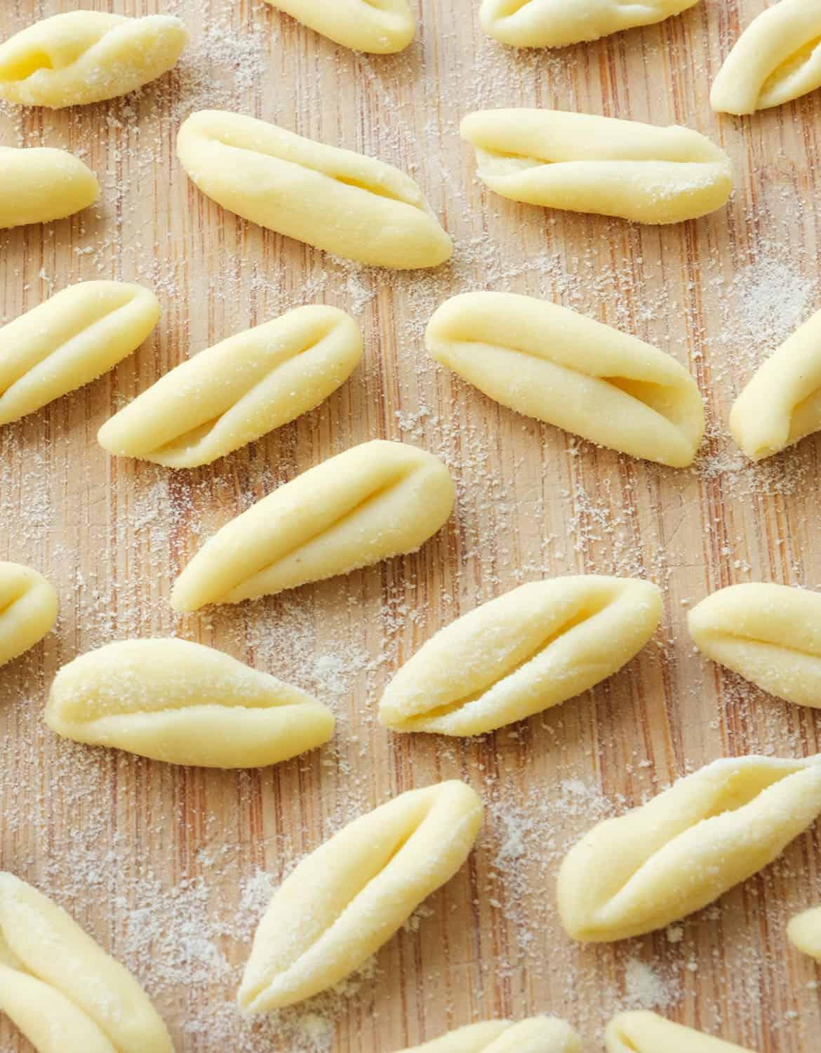 Image of a brown wooden table dusted in flour covered in freshly rolled cavatelli pasta.