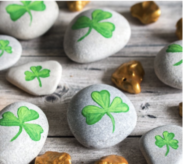 Three leaf clovers painted on round gray rocks.