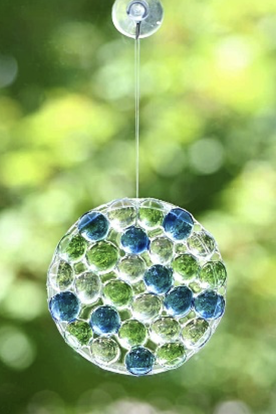 Glass bead blue and clear suncatcher over a background of blurred greenery