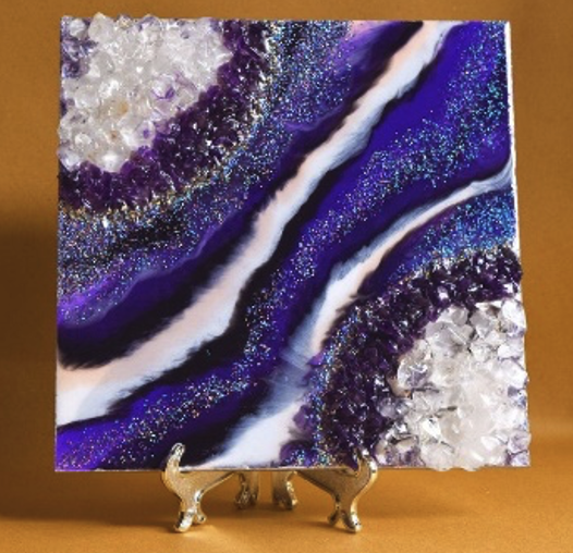 A slice of a blue, black, purple, and white geode placed on a silver stand.