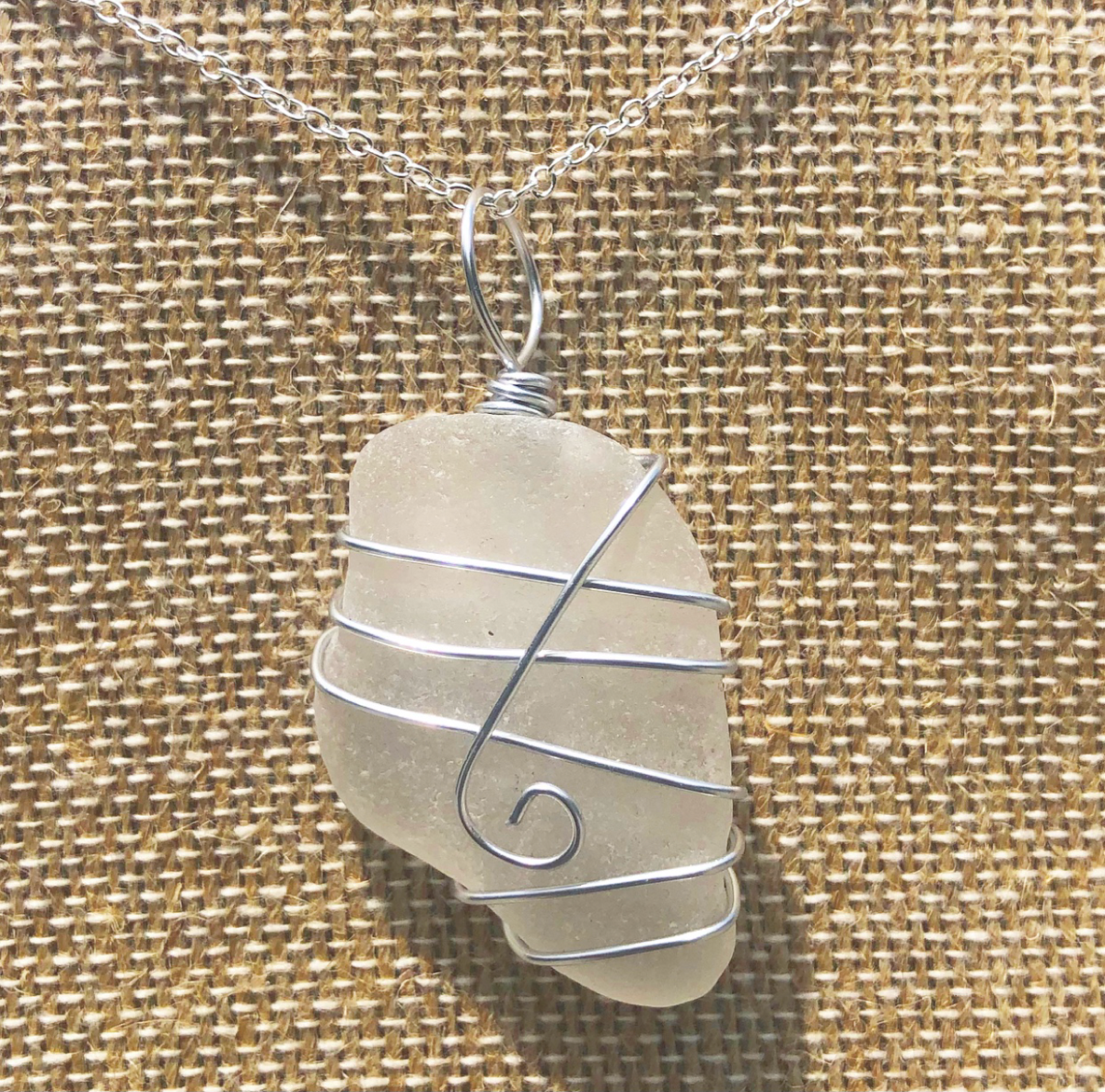 Image of a necklace with a piece of sea glass held onto the chain with a decorative twisted wire.