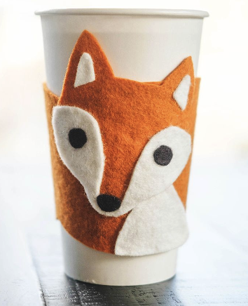 A fuzzy fox coffee cozy on a white coffee cup. 