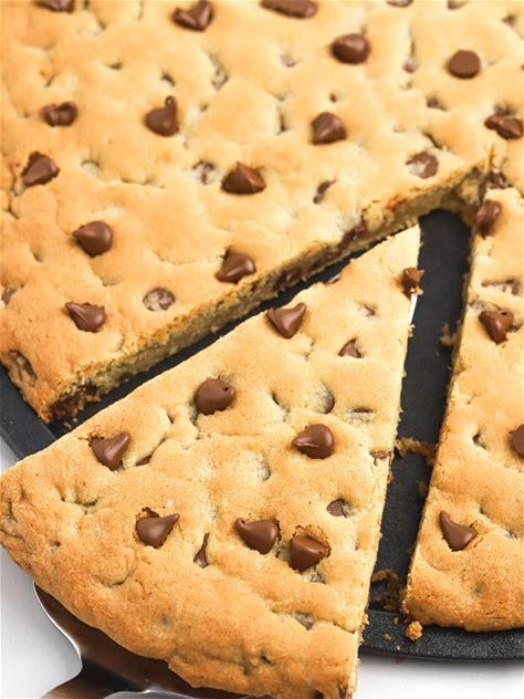 Image of a round pie made of chocolate chip cookie dough with a triangular slice cut out of it. 