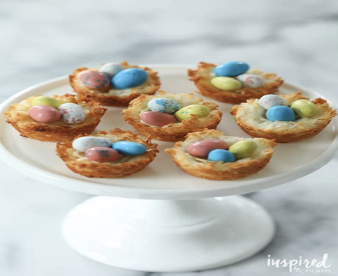 Coconut macaroon nests with chocolate eggs in them on a white plate.
