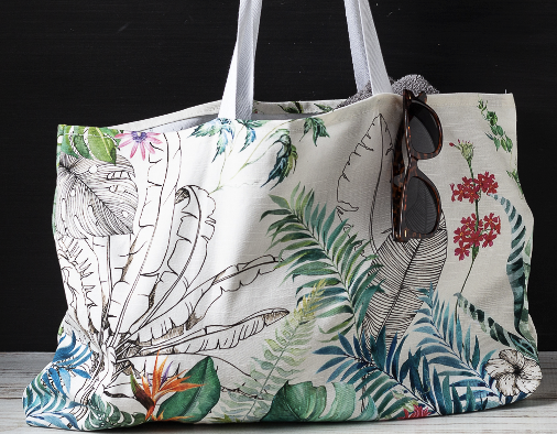 Beach bag with plants on it, and brown sunglasses hanging off of it.